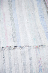 Textured flatweave of a vintage rag rug, showing recycled textile strips and pastel stripes with a central seam.