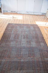 Distressed Belouch carpet texture highlighting elongated cartouches in copper orange and charcoal brown.