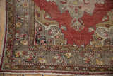 Distressed vintage Oushak rug corner showing worn red field and patterned grey-gold border.