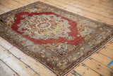 Distressed Turkish Oushak rug corner showing cinnabar red field, detailed border, and fringe.