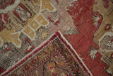 Distressed hand knotted Oushak rug corner, showing muted red pile and patterned border.