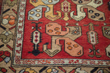 Rectilinear tribal pinwheel boteh motifs in peach, yellow, and blue on madder red Oushak.