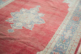 Distressed cherry red Oushak rug field revealing a grey star medallion and blue floral border.