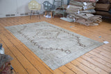 Angled view of distressed vintage Oushak rug, showing geometric brown outlines and arrow motifs.