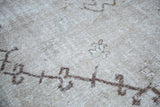 Distressed Oushak carpet showing light texture, brown pattern outlines, and subtle blue-green details.