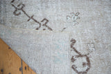 Distressed Oushak carpet's worn beige pile, brown patterns, and hand-knotted foundation with subtle blue threads.
