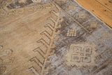 Distressed Oushak carpet with worn geometric patterns in earthy brown and charcoal.