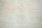 Distressed Oushak carpet texture with faded peach, ivory, and subtle green hues.