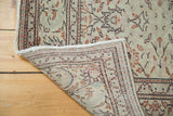 Distressed Kaisary carpet's folded corner reveals faded floral design and sturdy hand-knotted backing.