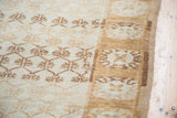 Distressed ivory Oushak carpet with repeating gold and bronze shadow floral patterns.