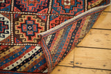 Kurdish runner folded, revealing vibrant red and blue gul patterns and striped woven foundation.