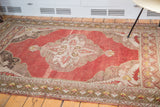 Distressed Oushak rug corner: cinnabar red field with abrash and ivory, bronze-toned spandrels.