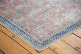 Distressed Turkish Kaisary carpet corner, showing burnt raspberry floral field and navy blue checkered border.