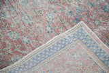 Distressed Kaisary carpet corner reveals worn floral pile and faded blue checkered border.