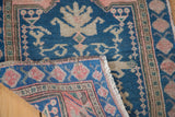 Folded corner of vintage Oushak rug reveals teal blue pile, dusty rose spandrel, and fringe.
