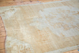 Fringed corner of distressed Oushak carpet, showing faded tribal patterns in muted tones.