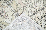 Distressed Oushak rug corner, revealing muted geometric pile and woven hand-knotted foundation.