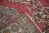 Hand-knotted distressed Oushak rug corner, featuring brick red, grey, and muted gold tribal patterns.