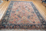 Distressed Heriz carpet corner with faded brick red field, navy samovar border, and ivory fringe.