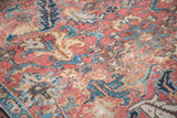 Distressed Heriz carpet with brick red, blue, gold and pastel floral motifs.