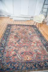 Distressed Heriz carpet corner with navy samovar border and brick red field's faded floral design.