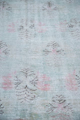 Vintage Oushak rug with distressed texture showing abstract floral patterns in muted lime green, light red, and charcoal.