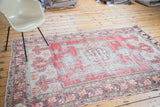 Distressed Turkish Oushak rug with faded cinnabar red, ivory, saffron, and floral rams horn motifs.