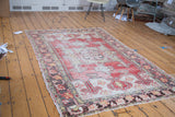 Faded cinnabar red, ivory, saffron floral designs on a distressed Oushak rug corner.