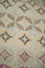 Distressed pile of modern abstract Oushak rug, with diamond motifs in gold, brown, and blush pink.