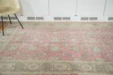Faded cranberry field with distressed grey-green floral Oushak pattern and abstract border.