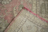 Distressed Oushak carpet, folded corner reveals faded cranberry floral pile and hand-knotted beige foundation.