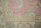 Distressed Oushak carpet texture with faded cranberry floral motifs and abstract grey-green border.