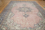 Distressed Oushak carpet featuring faded blush rose tones and muted charcoal medallion designs.