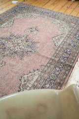 Distressed blush rose Oushak field with ornate faded charcoal border pattern.