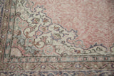 Distressed hand knotted Oushak rug corner, showing faded blush rose and intricate charcoal motifs.