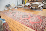 Distressed vintage Oushak runner displaying repeating geometric tribal medallions and faded red hues.