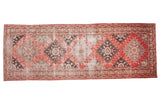 Distressed Oushak runner rug featuring tribal geometric medallions in faded reds and grey.