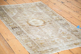 Textured distressed Oushak rug displaying central medallion, tendrils, and faded neutral colors.