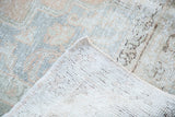 Folded corner of distressed Oushak carpet, revealing light woven foundation and soft peach, silver pile.