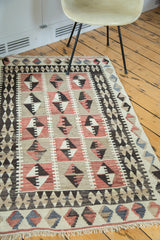 Distressed hand-woven Kilim rug featuring faded red, ivory, and charcoal black diamond motifs.