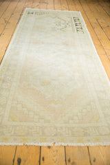 Distressed Turkish Oushak runner with faded ivory, apricot, and saffron geometric patterns.