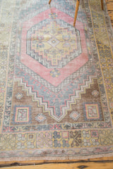 Distressed Oushak rug with faded pink, brown, and charcoal geometric border and fringe.