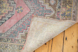 Folded distressed Oushak rug revealing light foundation, fringe, and faded cinnabar, grey, gold pile.