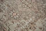 Distressed texture and muted ivory, rose, and grey floral patterns of an Oushak rug.