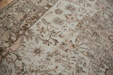 Distressed Oushak carpet featuring faded ivory, rose, and brown curvilinear motifs.