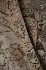 Distressed Oushak carpet's folded texture, showcasing light rose, ivory, and charcoal patterns.