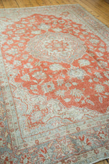 Distressed Oushak carpet corner shows faded cranberry field and soft grey border.