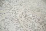 Distressed Oushak carpet texture with expressive charcoal floral outlines on faded ivory and green.