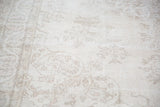 Detail of hand-knotted Oushak rug with beige and ivory field, subtle pastel plant motifs.