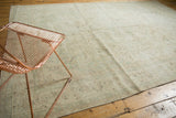 Faded celadon green, bronze, and ivory floral patterns at the edge of the hand knotted rug.
